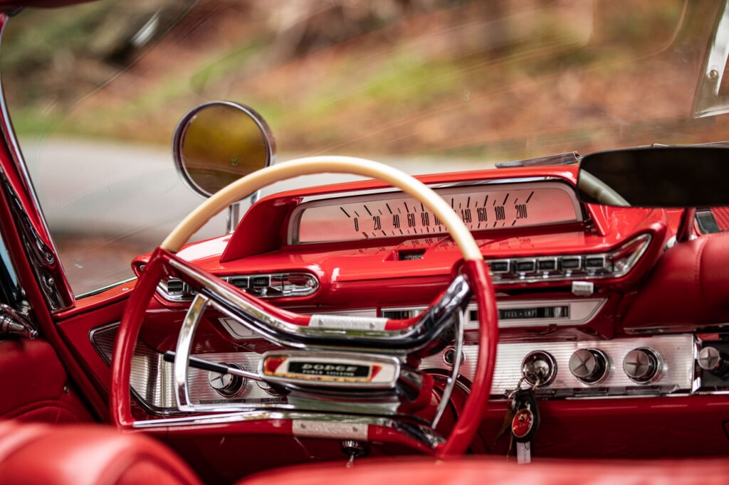 Close-up van het levendige rode interieur van een klassieke Dodge Polara, met het crèmekleurige stuurwiel, het chromen dashboard en de snelheidsmeter.