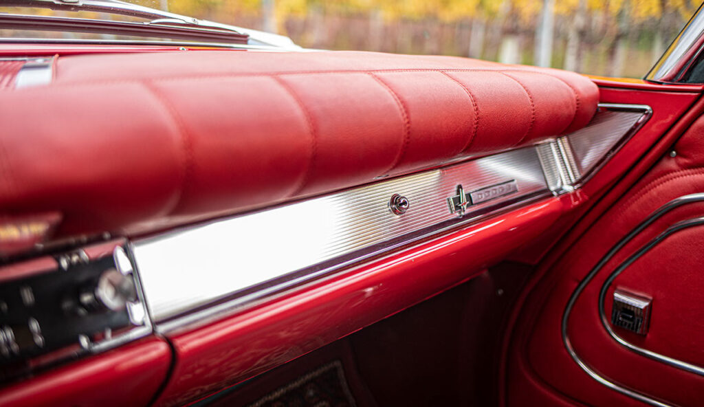 Close-up van het weelderige rode lederen dashboard en de passagierszijde van een Dodge Polara, met chromen accenten en een handschoenenkastje.