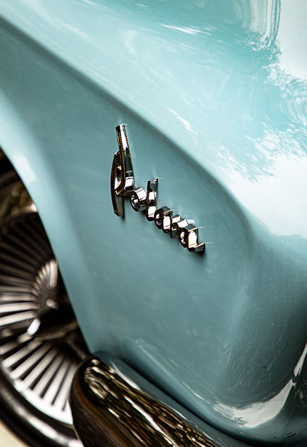Close-up van het chromen "Polara" embleem op de zijkant van een lichtblauwe klassieke Dodge Polara, met een glimp van het wiel en de bumper.