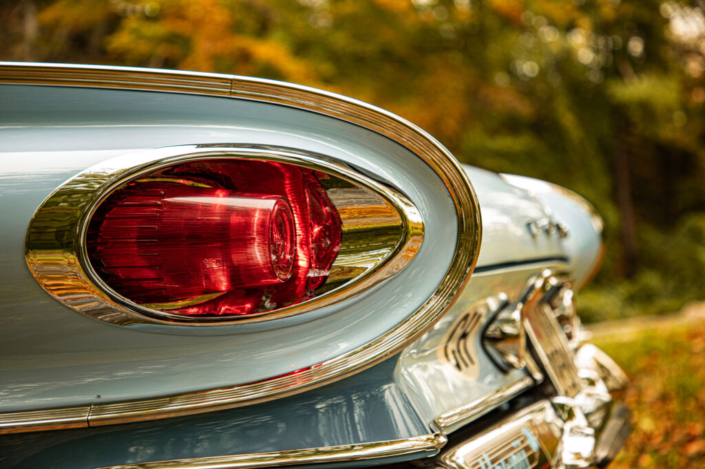 Close-up van het opvallende rode, ovale achterlicht van een lichtblauwe klassieke auto, omringd door dik chroom, met een onscherpe herfstachtige achtergrond.