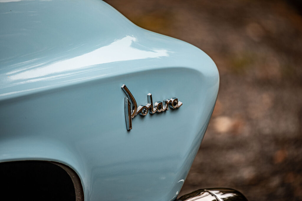 Close-up van het woord "Polara" in chroomletters op de lichtblauwe carrosserie van een Dodge Polara.